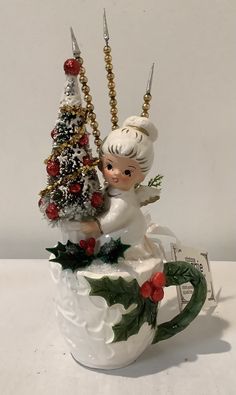 a ceramic figurine holding a christmas tree on top of a cup with holly