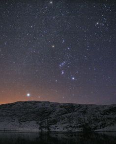 the night sky is filled with stars and bright lights over a mountain range, reflecting in water