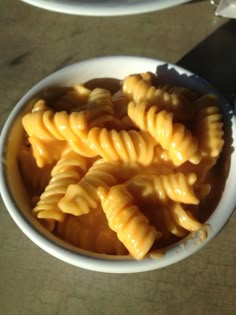 some pasta in a white bowl on top of a table next to a black knife