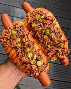 two hot dogs with toppings on them being held by someone