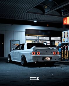 a white car is parked in front of a gas station with its lights on at night