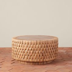 a round wooden table with woven wicker on the top, sitting on a tiled floor