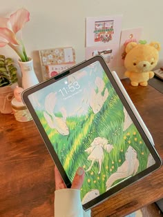 a person holding up an ipad with fairy images on the screen, and a teddy bear next to it