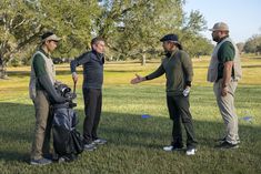 three men are standing in the grass talking to each other and holding golf club bags