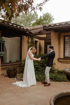 a bride and groom holding hands in front of a house with an outdoor fountain on the patio