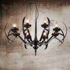 a chandelier with five lights hanging from it's center, in front of a concrete wall