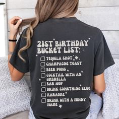 a woman wearing a 21st birthday bucket list t - shirt sitting on a bed with her back to the camera