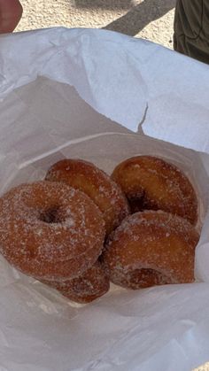 three sugared donuts in a paper bag on a table with someone's hand