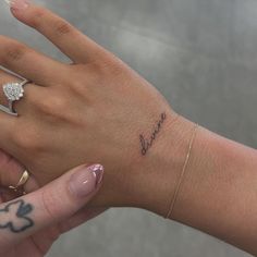 a woman's hand with a small diamond ring on her left wrist and the word love written in cursive writing