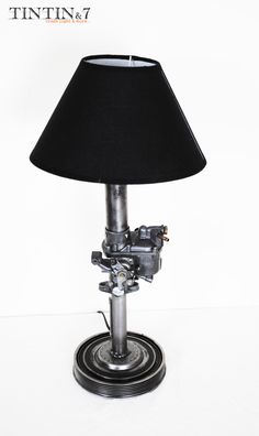 a lamp that is sitting on top of a metal base with a black shade over it