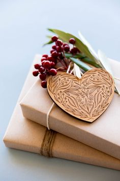 two wrapped gift boxes with wooden hearts on them and holly leaves sticking out of the top