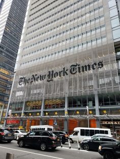 the new york times building is surrounded by tall buildings and parked cars in front of it