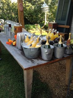 several buckets filled with drinks sitting on top of a wooden table in front of a house