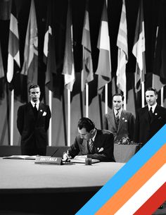 a group of men standing around a table with papers and pens in front of them