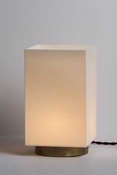 a white square lamp sitting on top of a table next to a black cord that is plugged in