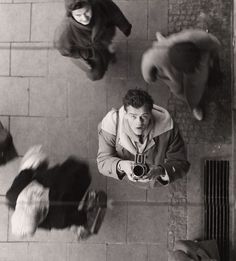 black and white photograph of man with camera surrounded by other men on the street, from above