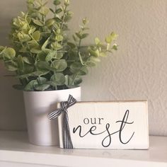 a potted plant sitting on top of a white shelf next to a sign that says our nest