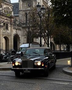 a black car driving down a street next to a tall building with a clock on it's face