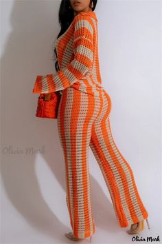 a woman in an orange and white knitted jumpsuit holding a handbag while standing next to a wall