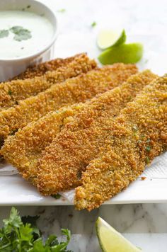 fried fish fillets on a white platter with lime wedges next to it