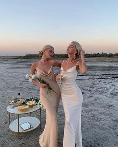 two beautiful women standing next to each other in front of a table with flowers on it