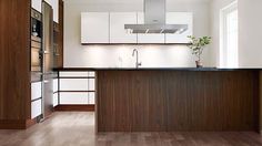 an empty kitchen with wood floors and white cabinetry, along with a stainless steel range hood