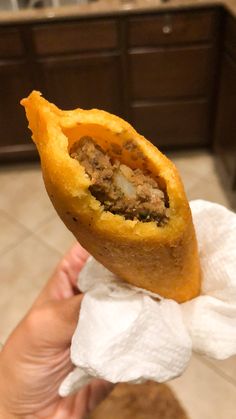 a person holding up a pastry with meat and cheese on it in a kitchen area