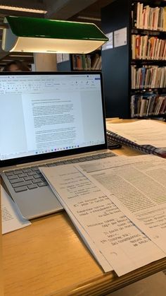 an open laptop computer sitting on top of a wooden desk next to bookshelves