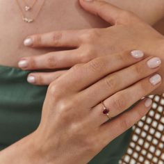 a woman wearing a gold ring with a red stone on her left hand and a green dress shirt