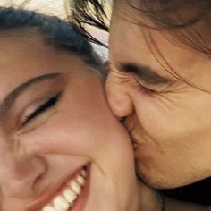 a man and woman kissing each other with their heads close to one another while smiling at the camera