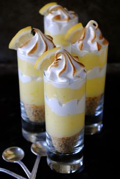 three desserts with lemon slices and whipped cream on top are sitting in small glasses