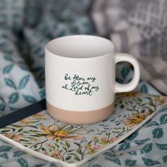 a coffee cup sitting on top of a bed next to a book and blanket with writing on it