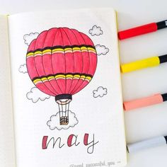 an open notebook with colored markers next to it and a drawing of a hot air balloon