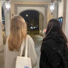 two women are walking down the street at night with shopping bags on their back legs