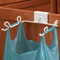 a blue bag hanging from the side of a wooden cabinet with two white hooks on it