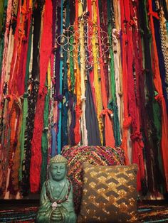 a buddha statue sitting on top of a colorful rug next to a pile of scarves