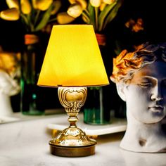 a yellow lamp sitting on top of a table next to a white busturine