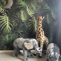 two stuffed elephants and a giraffe standing in front of a jungle wallpaper