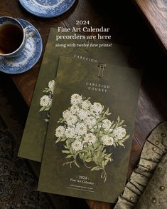 two pamphlets sitting on top of a wooden table next to a cup of tea and saucer