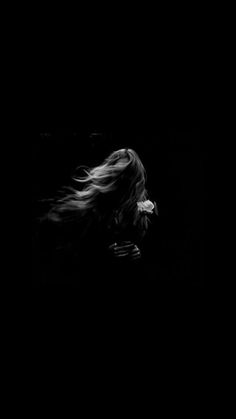 black and white photograph of woman with long hair blowing in the wind on dark background