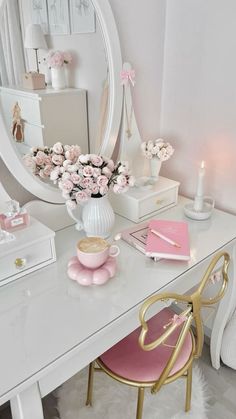 a white desk topped with a mirror next to a pink chair and vase filled with flowers