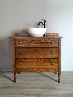 a bathroom sink sitting on top of a wooden dresser next to a white bowl under a faucet