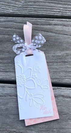 a white tag with pink ribbon hanging from it's side on a wooden surface