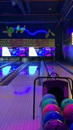 bowling balls are lined up in a bowling alley with neon lights on the wall behind them