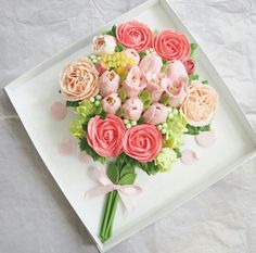 a bouquet of pink and orange flowers on a white tray with green leaves, buds and pearls