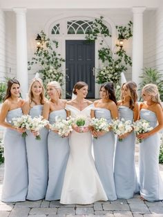 a group of women standing next to each other in front of a building with white flowers