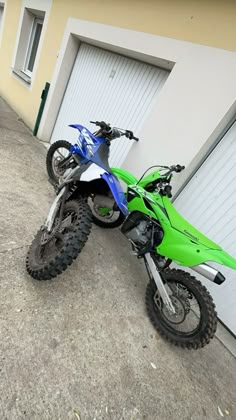 a green dirt bike parked in front of a garage with two doors on the side