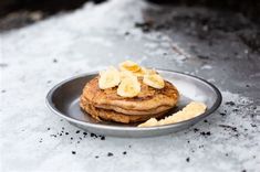 a stack of pancakes with banana slices on a metal plate in the middle of snow