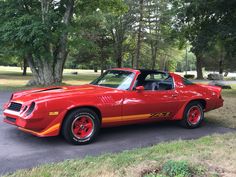 a red sports car parked on the side of a road in front of some trees