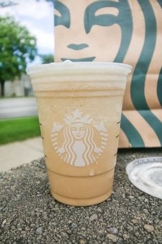 a starbucks cup sitting on the ground next to a paper bag